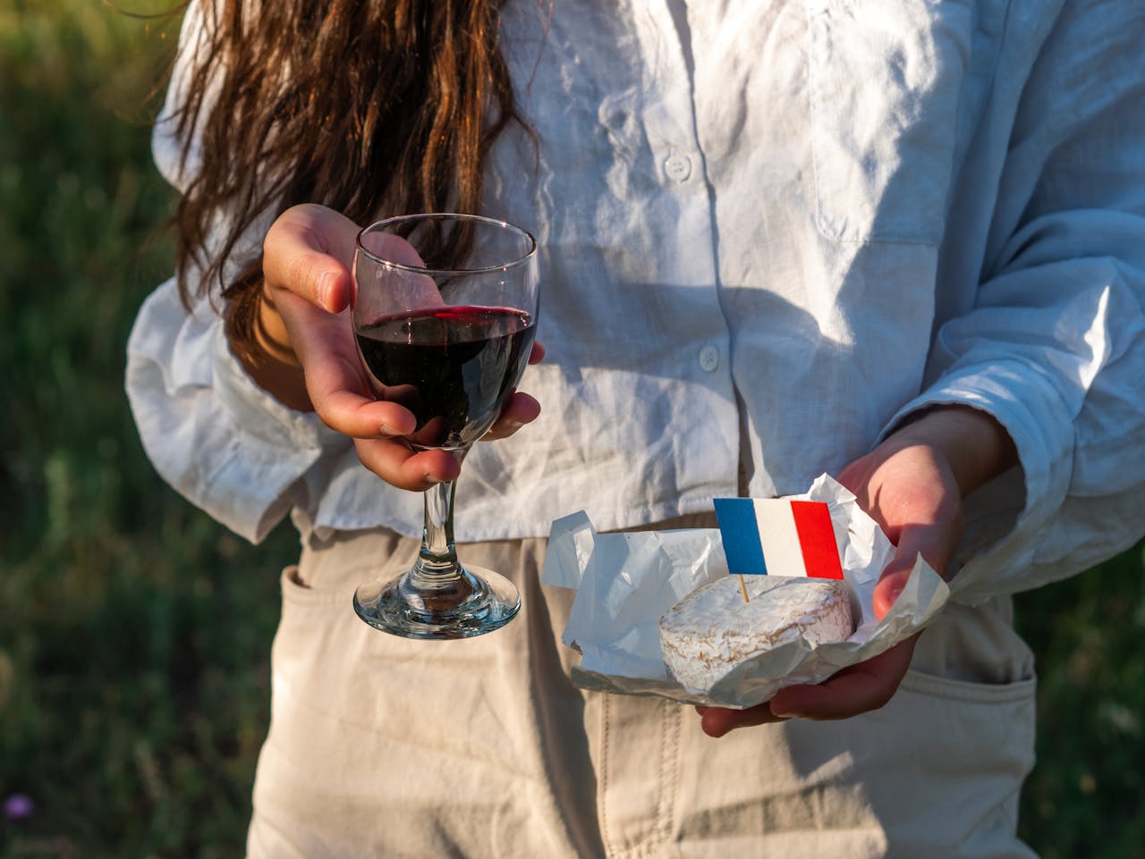 Woman holding a glass of red wine and camembert with French flag outdoors.