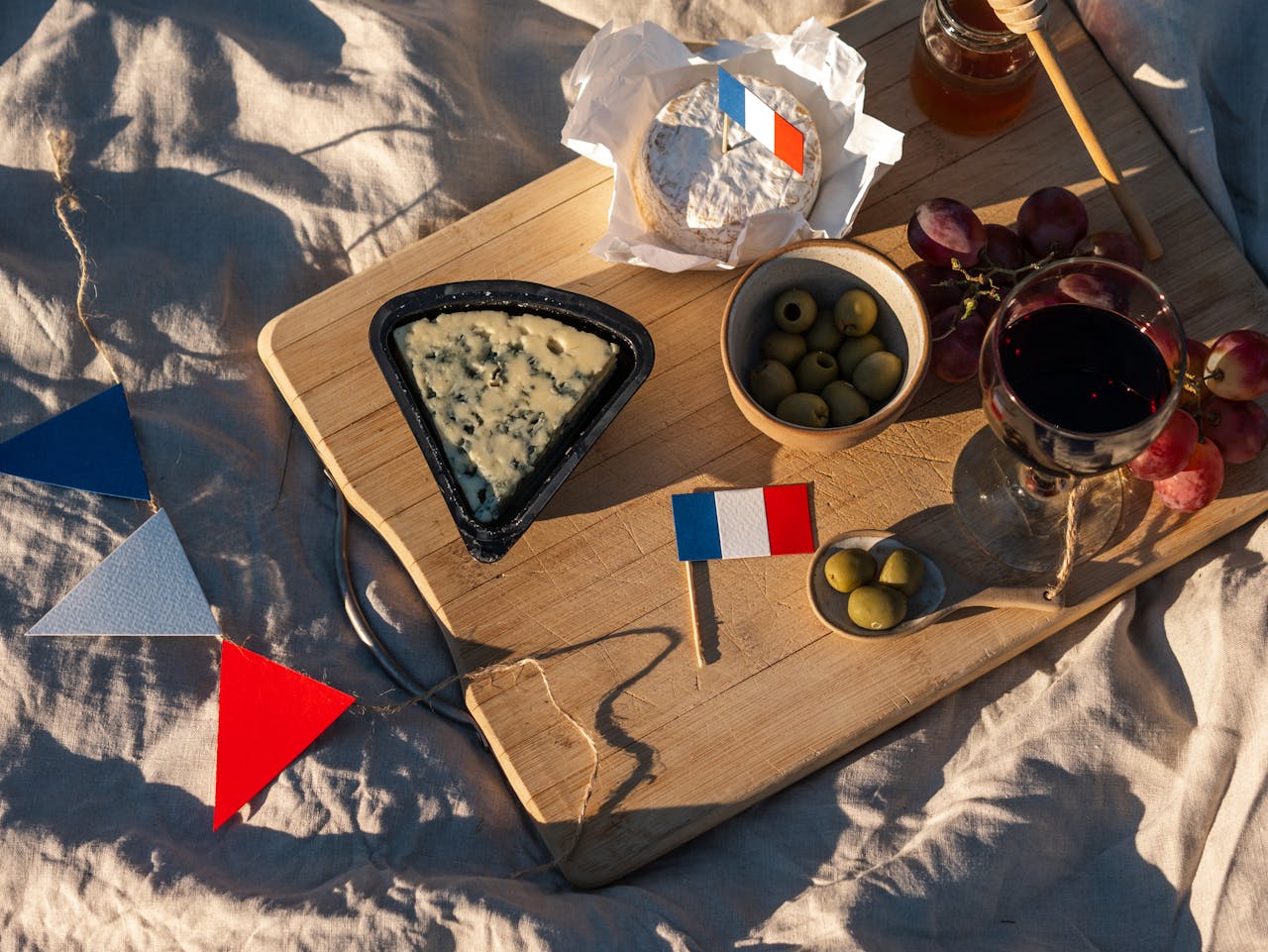 A rustic French picnic with wine, grapes, cheese, and a flag arranged on a wooden board.
