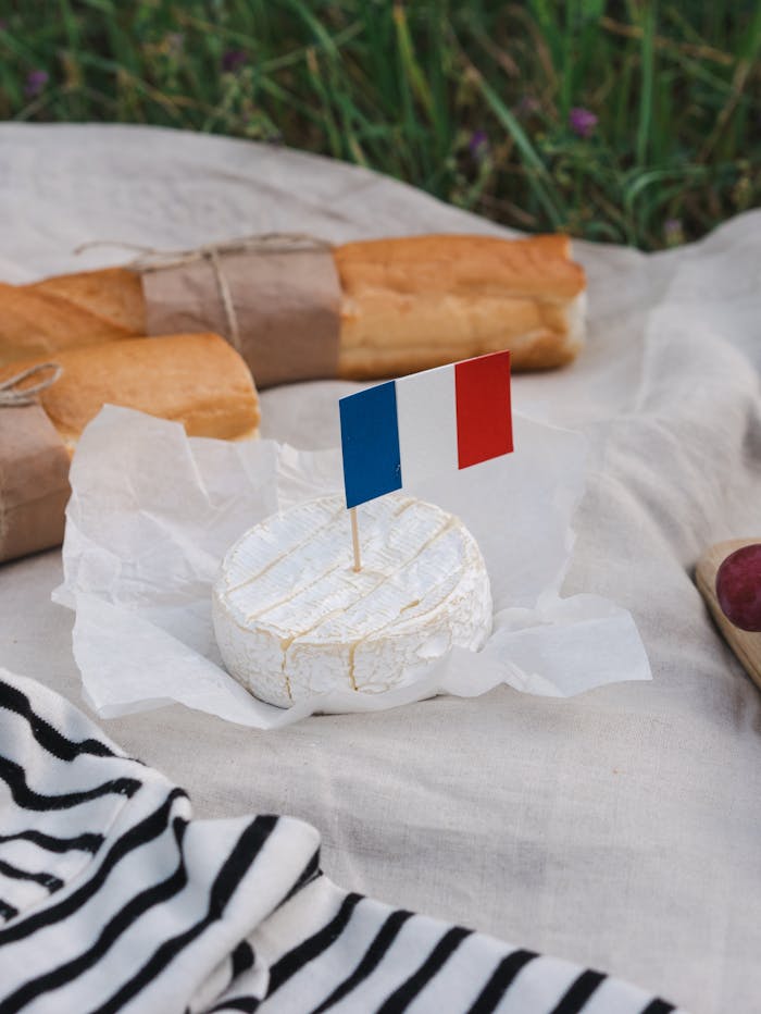 French picnic setup with camembert and baguettes on a cloth with French flag.